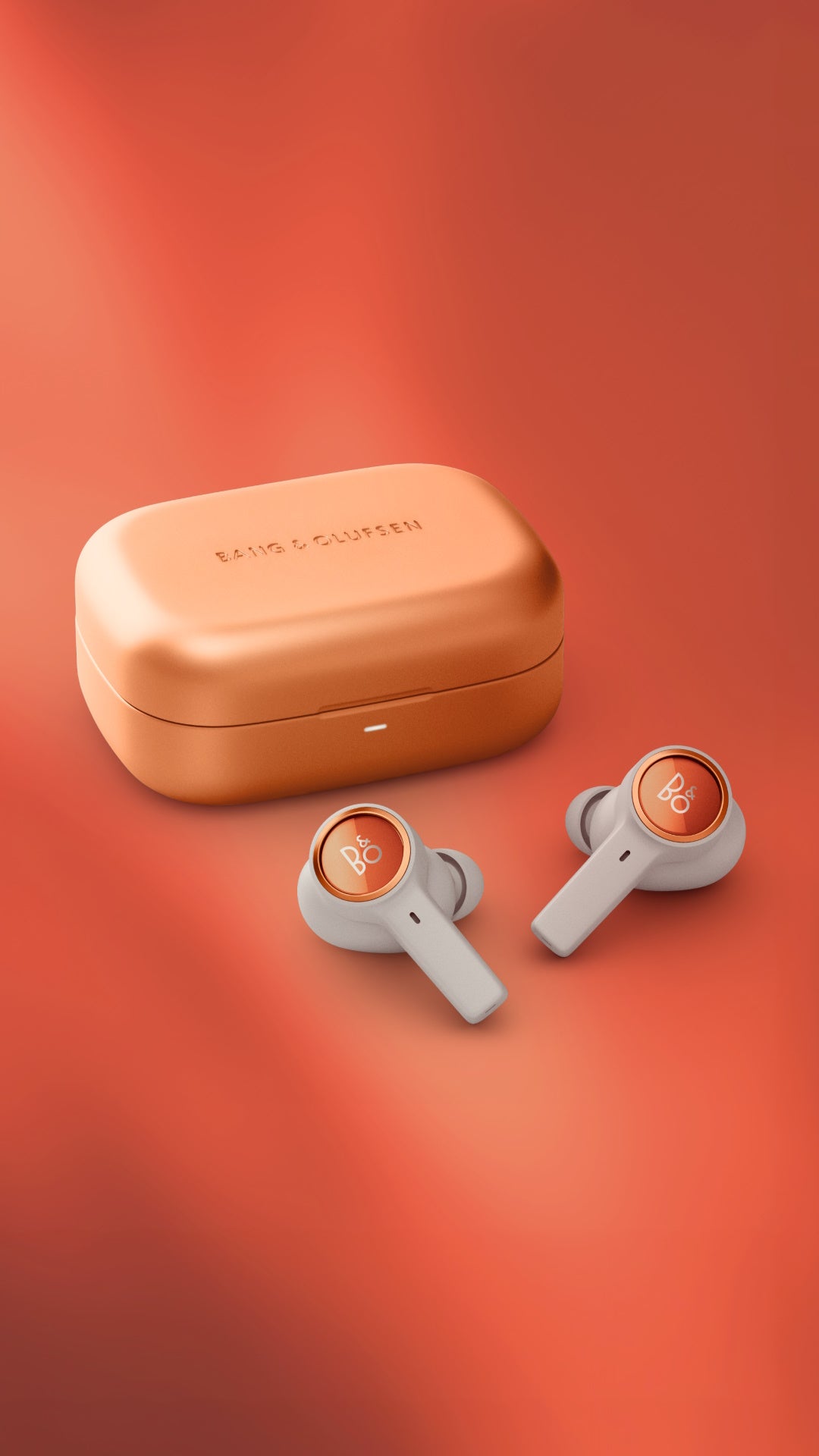 Studio-Aufnahme der Bang & Olufsen Beoplay Eleven In-Ear-Kopfhörer in der Farbe Dune. Die sandfarbenen Earbuds mit kupferfarbenem Aluminium-Ring liegen vor dem passenden, gravierten Aluminium-Ladecase auf einem farblich abgestimmten, warmen Hintergrund.