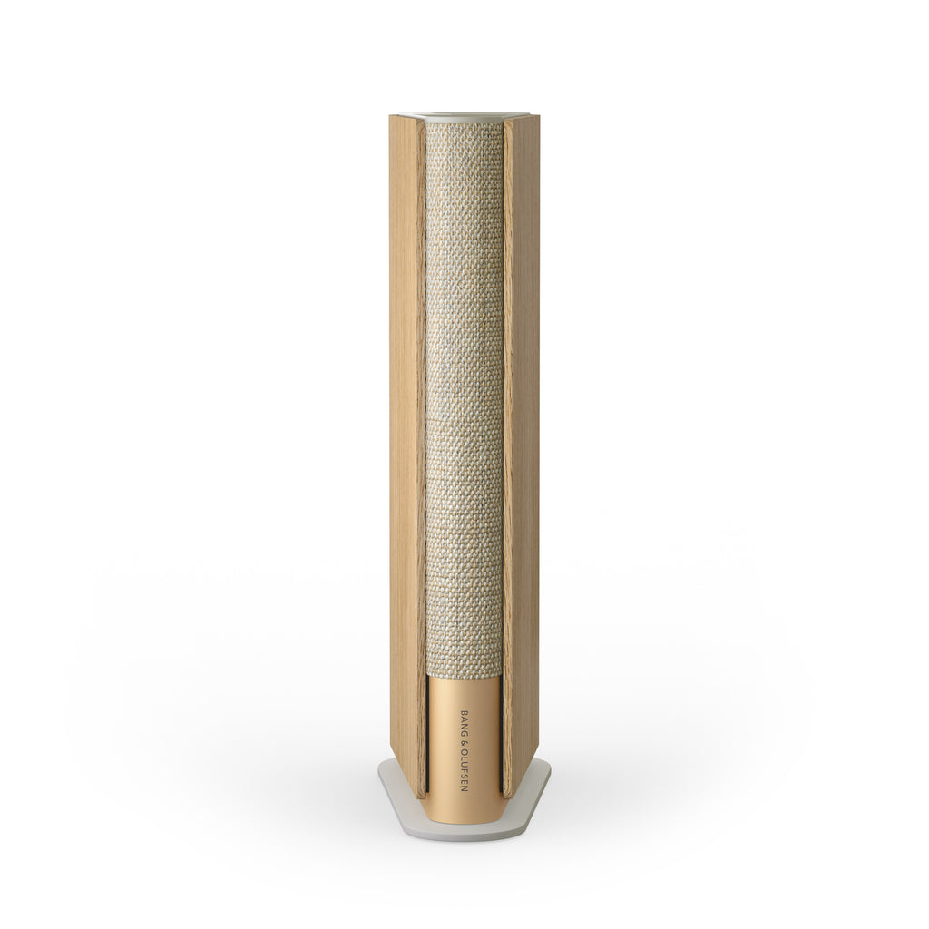 Vorderansicht der Bang & Olufsen Beosound Emerge in Gold Tone mit Seitenteilen aus heller Eiche. Der ultra-schlanke WLAN-Lautsprecher im eleganten Buch-Design kombiniert eloxiertes Aluminium, hochwertigen Textilstrick und Echtholz vor weißem Hintergrund.